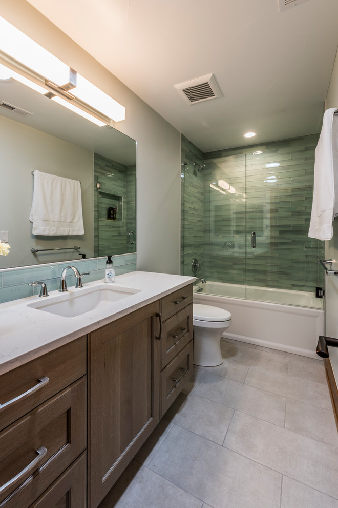 This is an example of a mid-sized transitional master bathroom in Denver with recessed-panel cabinets, dark wood cabinets, an alcove tub, a shower/bathtub combo, a one-piece toilet, blue tile, glass tile and an undermount sink.