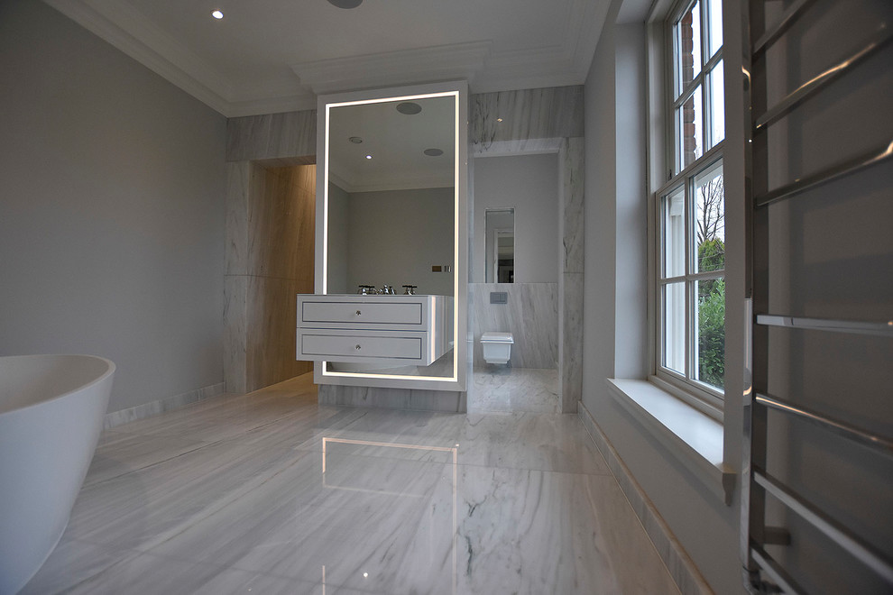 Photo of a large modern master wet room bathroom in Surrey with flat-panel cabinets, black cabinets, a freestanding tub, a wall-mount toilet, black and white tile, marble, black walls, marble floors, a drop-in sink, glass benchtops, multi-coloured floor, an open shower and black benchtops.
