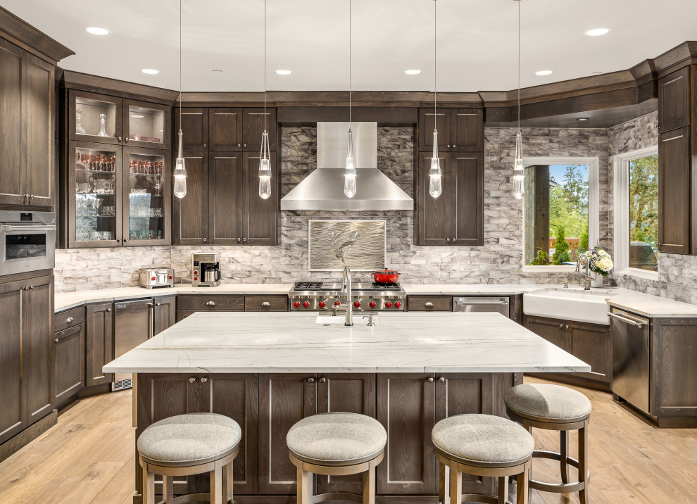 Photo of a large country u-shaped eat-in kitchen in Portland with a farmhouse sink, shaker cabinets, dark wood cabinets, quartzite benchtops, multi-coloured splashback, marble splashback, stainless steel appliances, light hardwood floors, multiple islands and grey benchtop.
