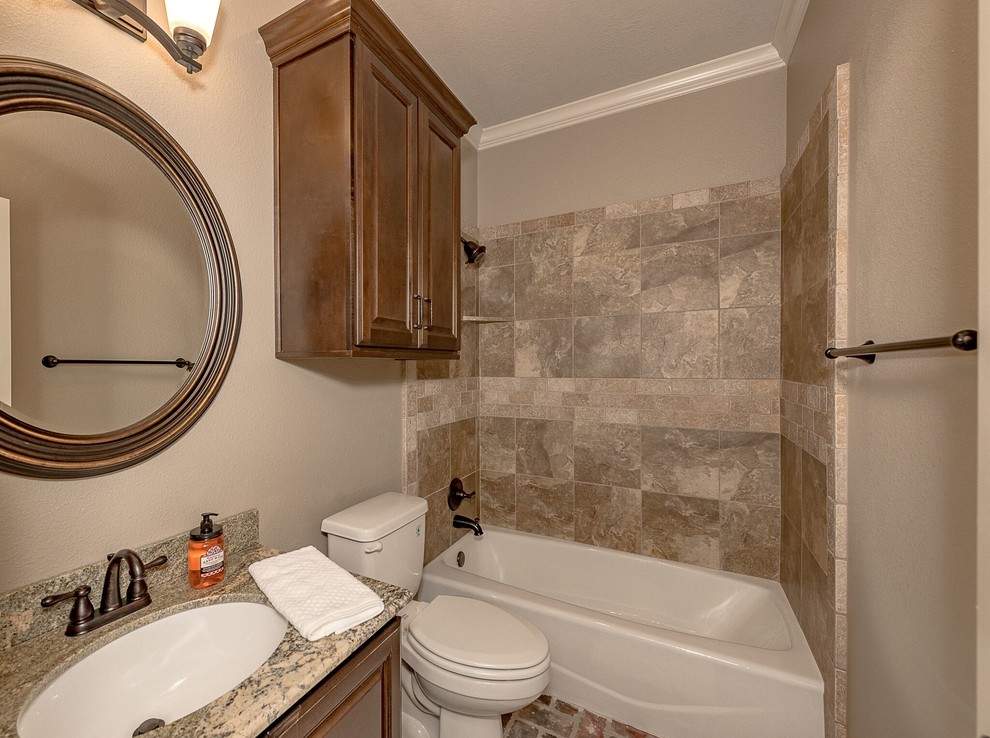 This is an example of a mid-sized country 3/4 bathroom in Austin with shaker cabinets, medium wood cabinets, an alcove tub, a shower/bathtub combo, a two-piece toilet, brown tile, travertine, beige walls, brick floors, an undermount sink, granite benchtops, brown floor and an open shower.