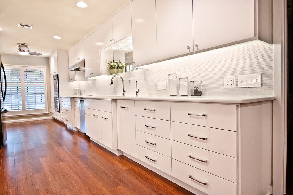 Photo of a modern galley eat-in kitchen in Austin with a farmhouse sink, flat-panel cabinets, white cabinets, granite benchtops, green splashback and glass tile splashback.