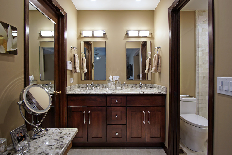 This is an example of a mid-sized traditional master bathroom in Chicago with recessed-panel cabinets, dark wood cabinets, an alcove shower, a one-piece toilet, beige tile, stone tile, beige walls, ceramic floors, an undermount sink and granite benchtops.