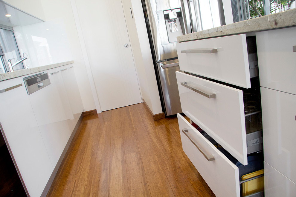 Photo of a mid-sized contemporary galley kitchen in Perth with granite benchtops, white splashback, glass sheet splashback, stainless steel appliances, bamboo floors and with island.