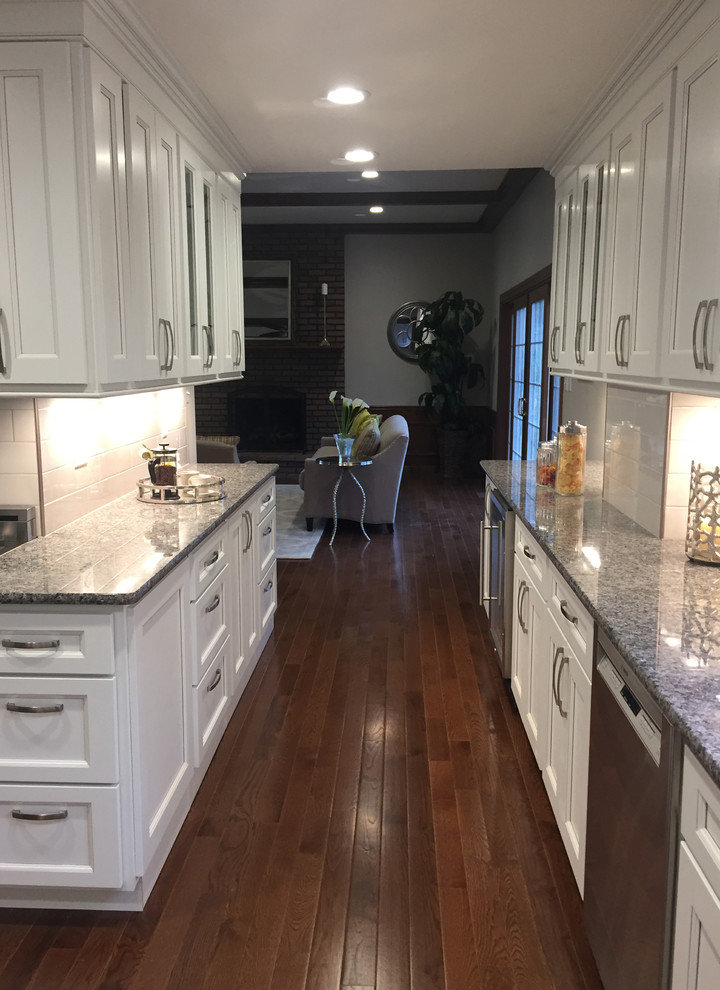 Inspiration for a transitional galley dark wood floor kitchen remodel with an undermount sink, flat-panel cabinets, white cabinets, granite countertops, white backsplash, porcelain backsplash, stainless steel appliances and an island