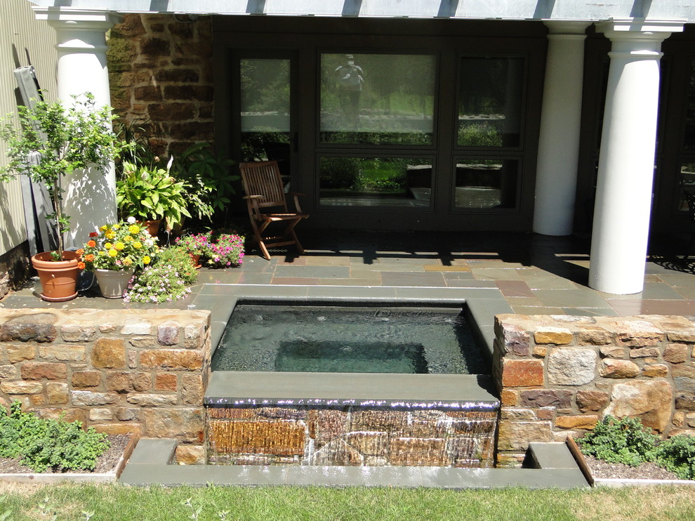 Design ideas for a small traditional courtyard rectangular infinity pool in Philadelphia with a hot tub and natural stone pavers.