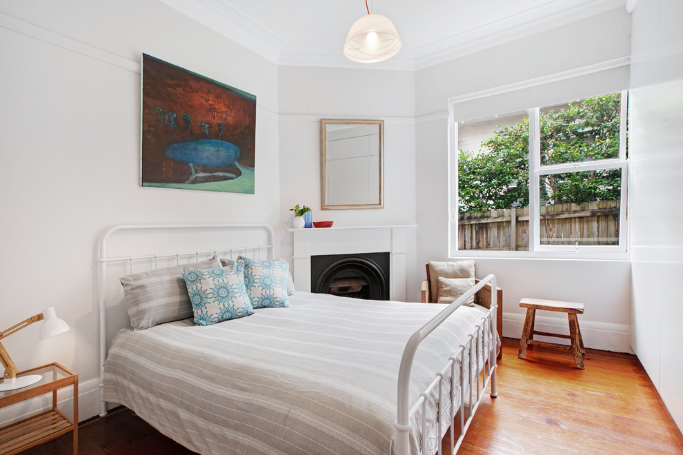 Design ideas for a transitional bedroom in Sydney with white walls, medium hardwood floors, a standard fireplace and brown floor.