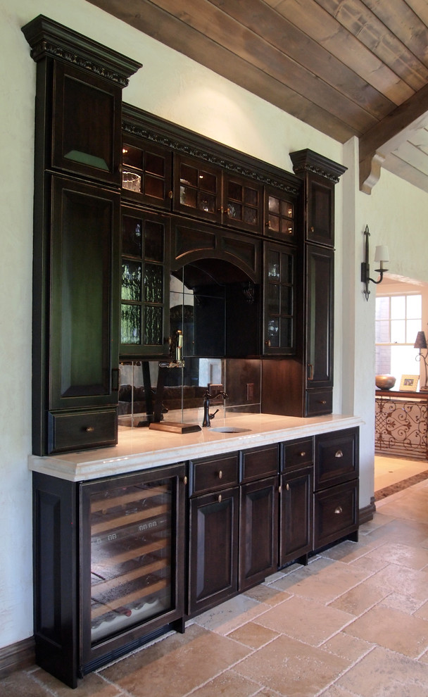 Design ideas for a mid-sized traditional single-wall wet bar in St Louis with an undermount sink, raised-panel cabinets, dark wood cabinets, granite benchtops, limestone floors and mirror splashback.