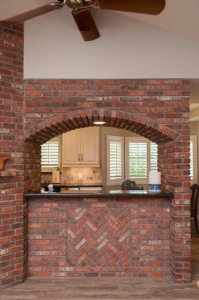 Mid-sized transitional galley porcelain tile and beige floor enclosed kitchen photo with a triple-bowl sink, raised-panel cabinets, white cabinets, granite countertops, beige backsplash, porcelain backsplash, stainless steel appliances and a peninsula
