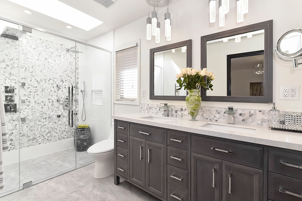 This is an example of a contemporary master bathroom in Calgary with recessed-panel cabinets, a double shower, gray tile, pebble tile, white walls, porcelain floors, marble benchtops and an undermount sink.