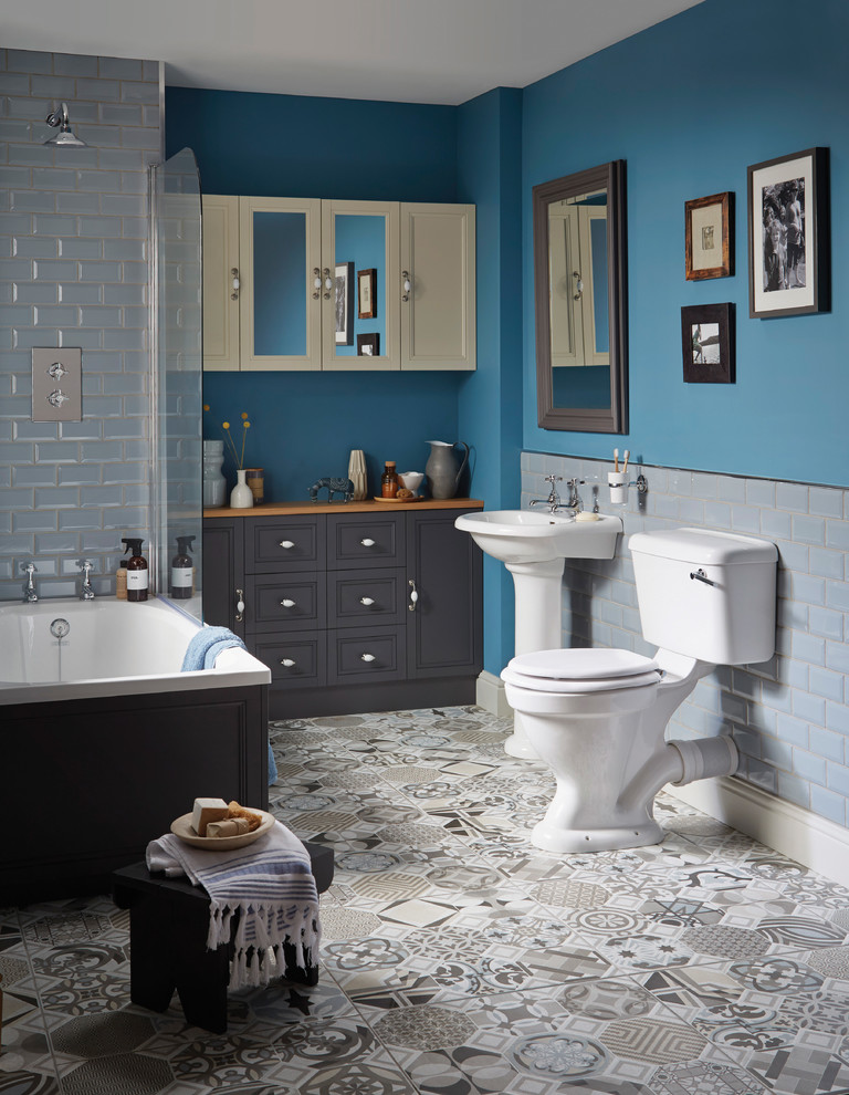 Inspiration for a traditional bathroom in West Midlands with recessed-panel cabinets, grey cabinets, a drop-in tub, a shower/bathtub combo, a two-piece toilet, blue tile, blue walls and a pedestal sink.