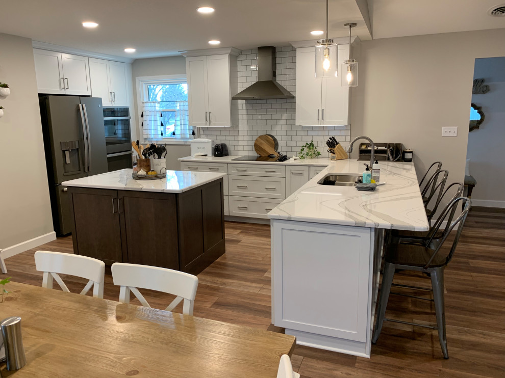 Inspiration for a large transitional u-shaped vinyl floor and brown floor open concept kitchen remodel with an undermount sink, shaker cabinets, white cabinets, quartz countertops, white backsplash, ceramic backsplash, stainless steel appliances, an island and white countertops