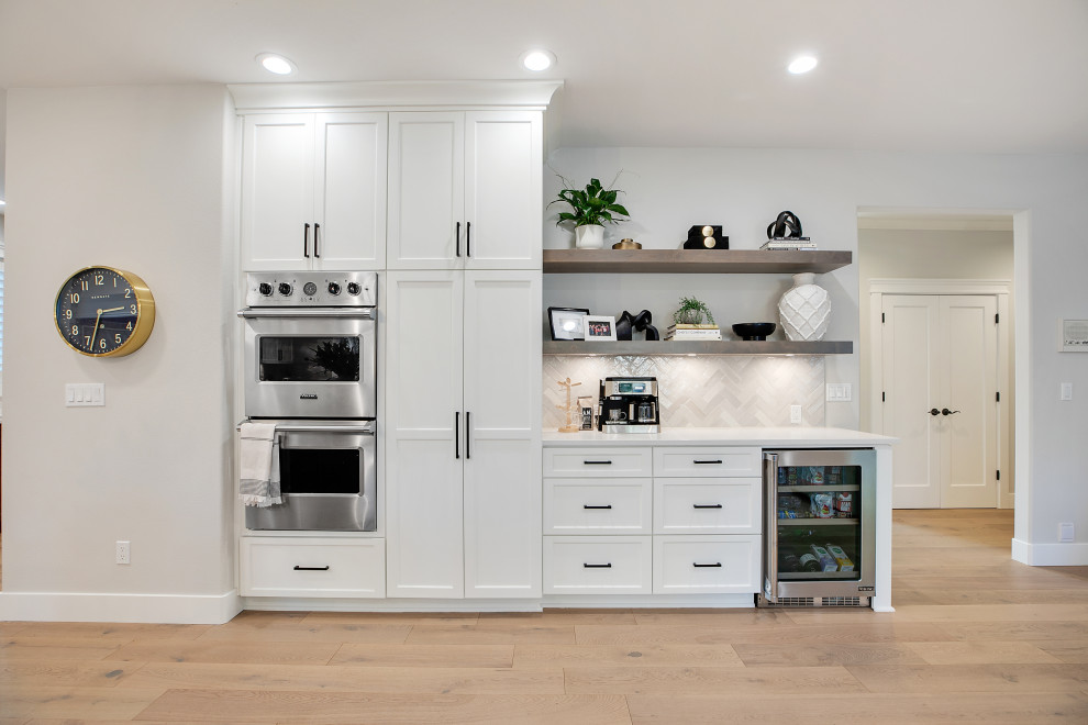 Modern inredning av ett mycket stort vit vitt kök, med en rustik diskho, skåp i shakerstil, vita skåp, bänkskiva i kvarts, vitt stänkskydd, stänkskydd i keramik, rostfria vitvaror, ljust trägolv, en köksö och brunt golv