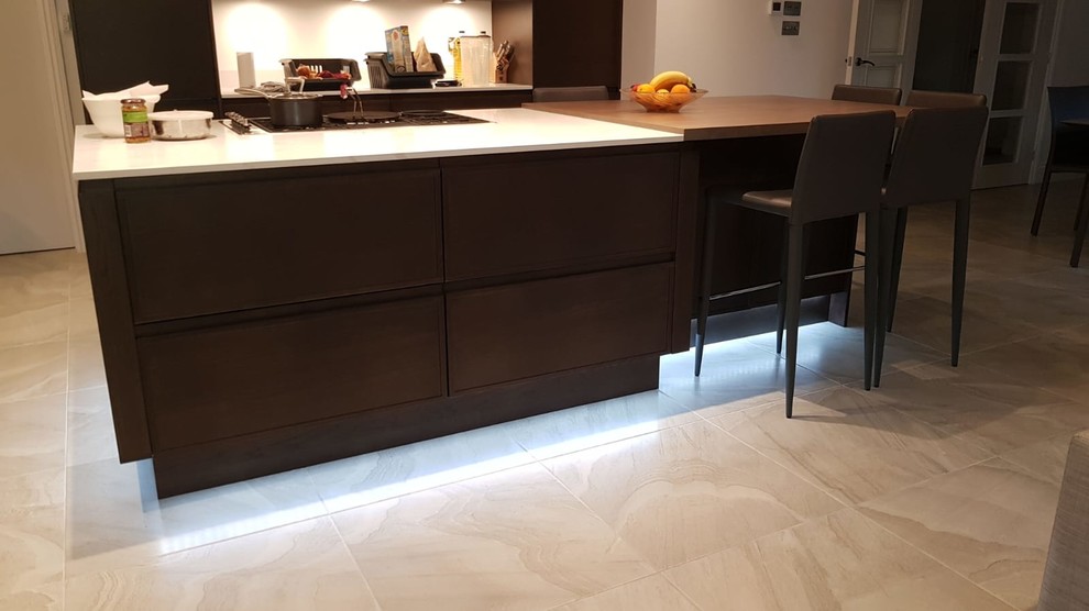 Photo of a mid-sized modern galley open plan kitchen in London with flat-panel cabinets, dark wood cabinets, quartzite benchtops, white splashback, marble splashback, black appliances, porcelain floors, with island, grey floor and white benchtop.