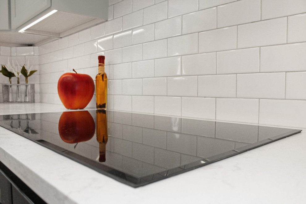 Example of a large transitional u-shaped light wood floor and brown floor enclosed kitchen design in Boston with a double-bowl sink, shaker cabinets, gray cabinets, quartz countertops, white backsplash, porcelain backsplash, black appliances, an island and white countertops