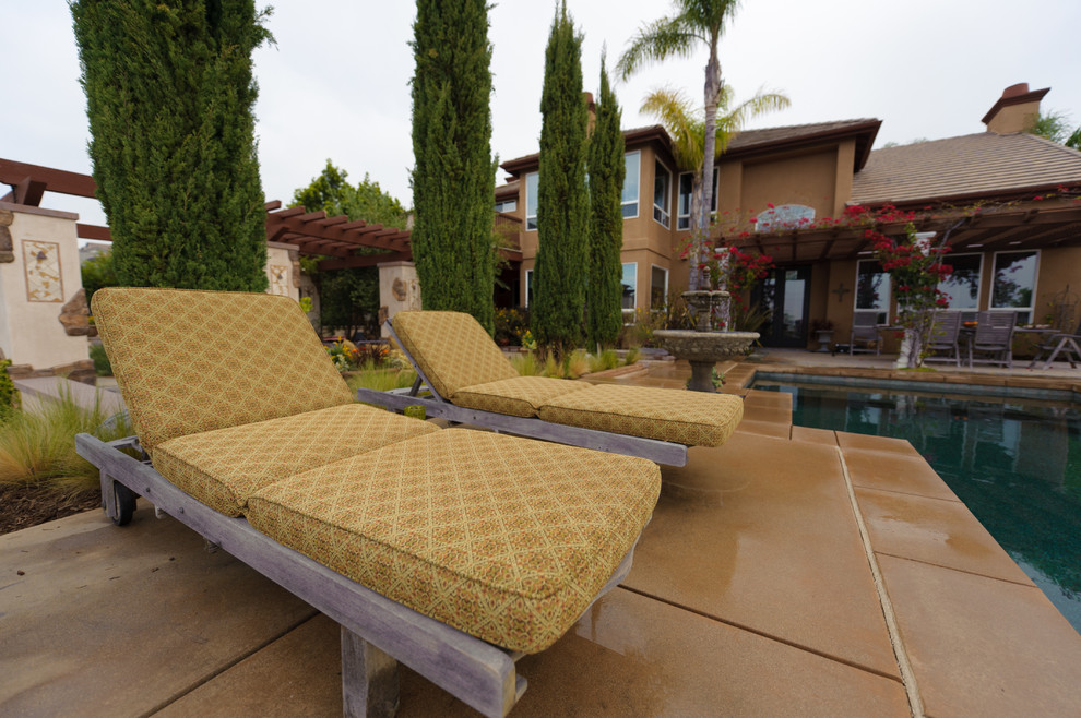 Immagine di una grande piscina a sfioro infinito mediterranea personalizzata dietro casa con fontane e lastre di cemento