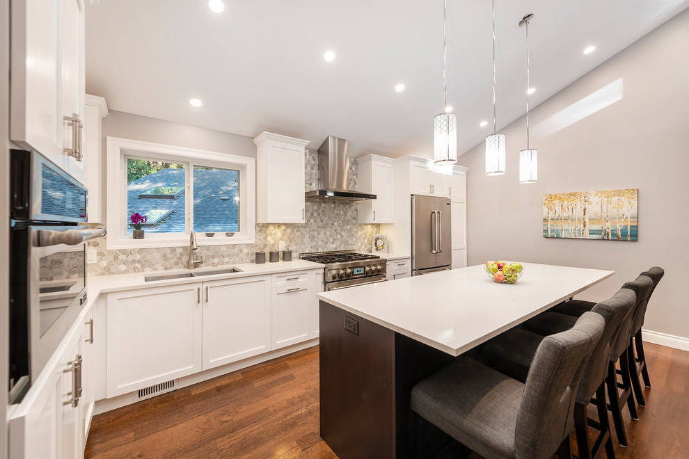 Large transitional l-shaped medium tone wood floor and brown floor eat-in kitchen photo in Vancouver with an undermount sink, shaker cabinets, white cabinets, quartzite countertops, multicolored backsplash, marble backsplash, stainless steel appliances, an island and white countertops