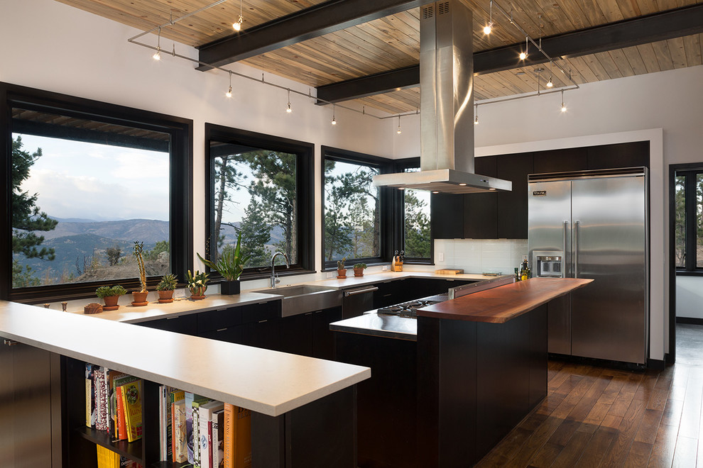 Example of a large minimalist u-shaped medium tone wood floor kitchen design in Denver with a farmhouse sink, flat-panel cabinets, black cabinets, marble countertops, white backsplash, stainless steel appliances and an island