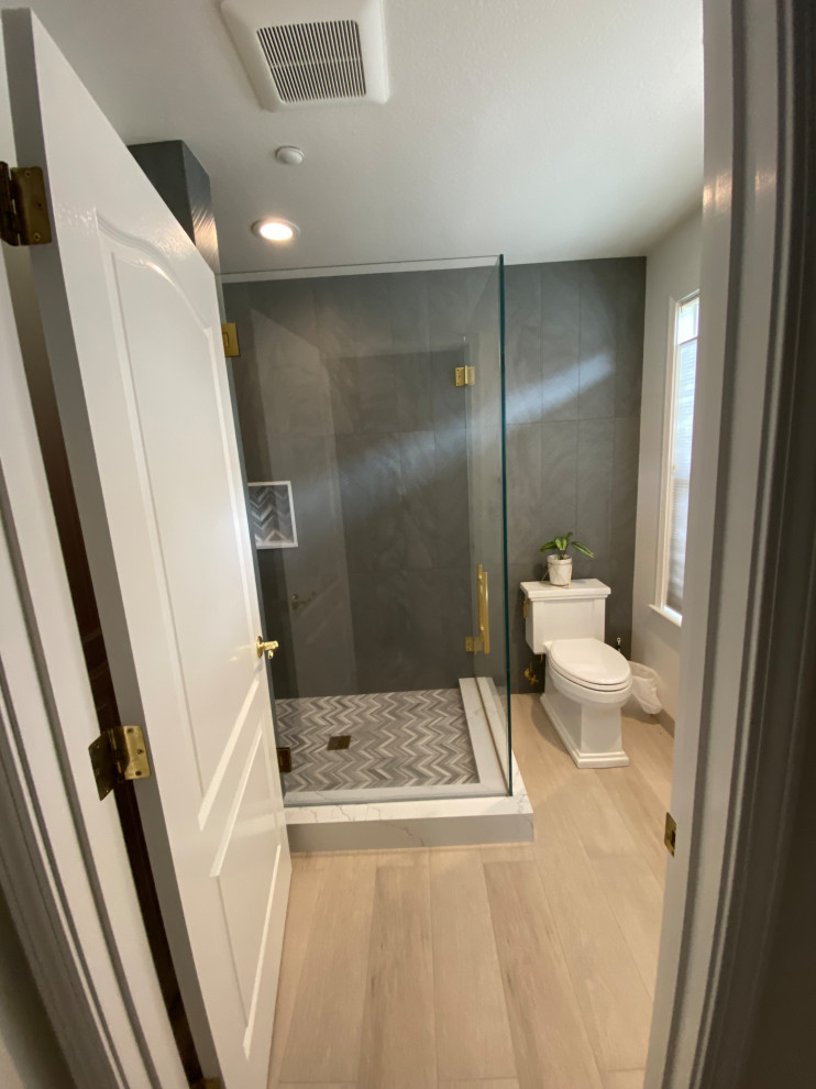 Example of a transitional light wood floor and single-sink corner shower design with a two-piece toilet, gray walls, a hinged shower door and a built-in vanity