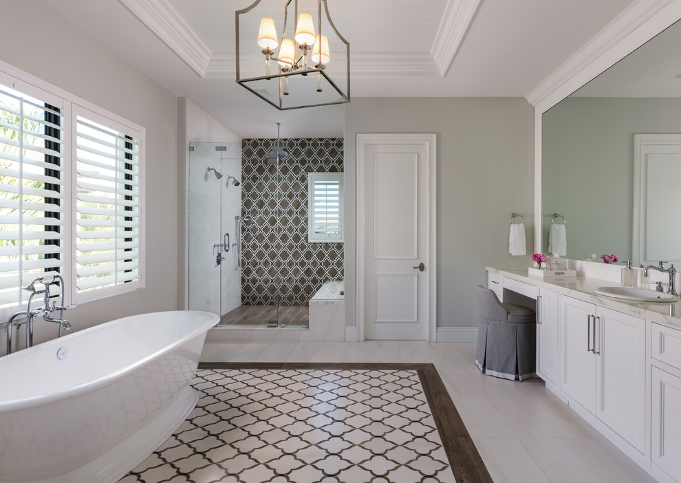 This is an example of a transitional master bathroom in Other with recessed-panel cabinets, white cabinets, a freestanding tub, a double shower, multi-coloured tile, grey walls, a drop-in sink, multi-coloured floor, a hinged shower door and white benchtops.