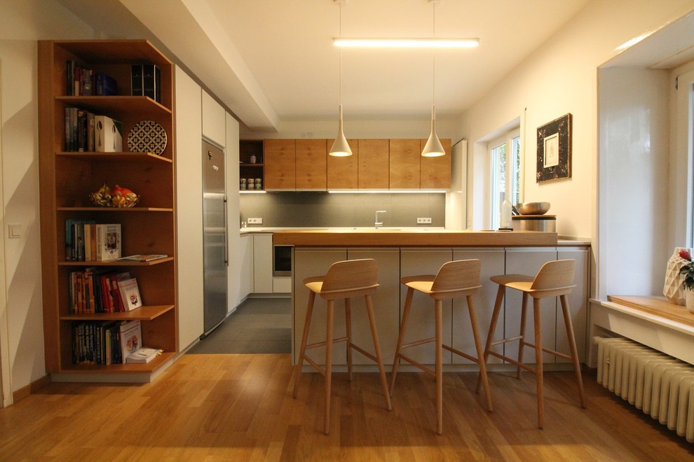 Große, Offene Moderne Küche in L-Form mit flächenbündigen Schrankfronten, Einbauwaschbecken, weißen Schränken, Arbeitsplatte aus Holz, Küchenrückwand in Weiß, Kalk-Rückwand, Küchengeräten aus Edelstahl, hellem Holzboden, Halbinsel und beigem Boden in Berlin