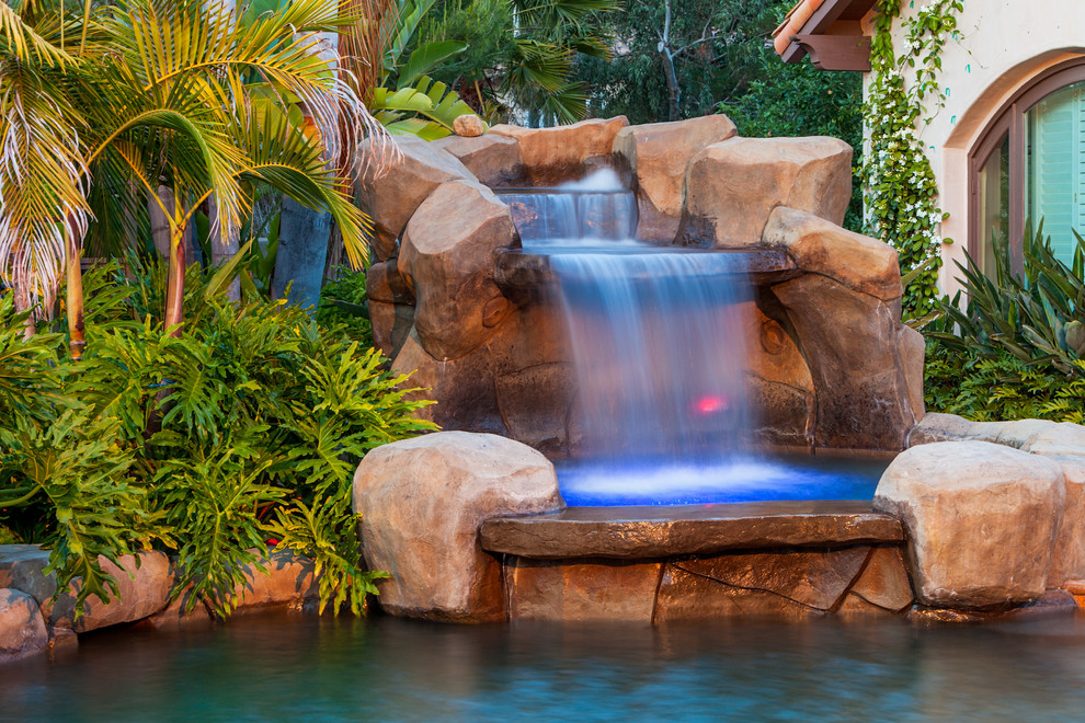 Expansive tropical backyard custom-shaped natural pool in San Diego with natural stone pavers and a water feature.