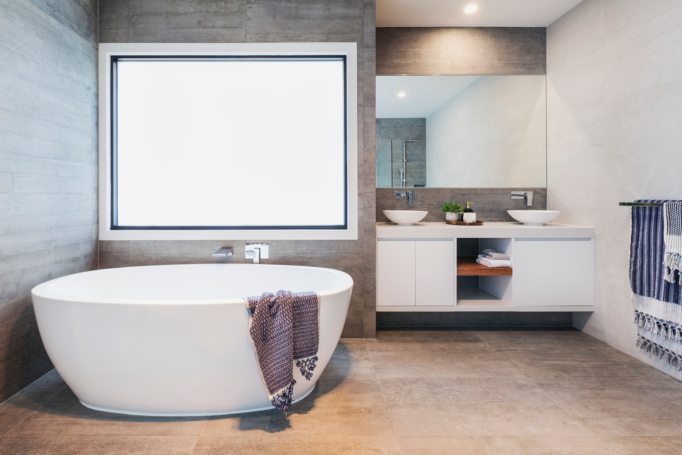 This is an example of a mid-sized contemporary master bathroom in Melbourne with flat-panel cabinets, white cabinets, a freestanding tub, an alcove shower, a two-piece toilet, gray tile, cement tile, grey walls, concrete floors, a vessel sink and engineered quartz benchtops.