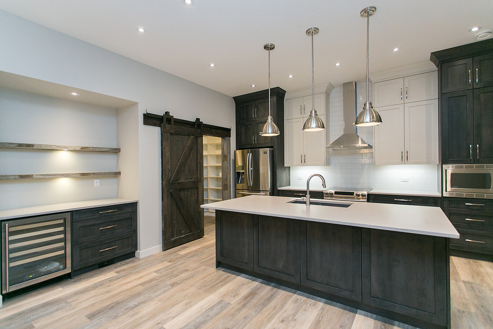 Design ideas for a mid-sized contemporary single-wall open plan kitchen in Calgary with an undermount sink, shaker cabinets, dark wood cabinets, solid surface benchtops, white splashback, subway tile splashback, stainless steel appliances, medium hardwood floors and with island.
