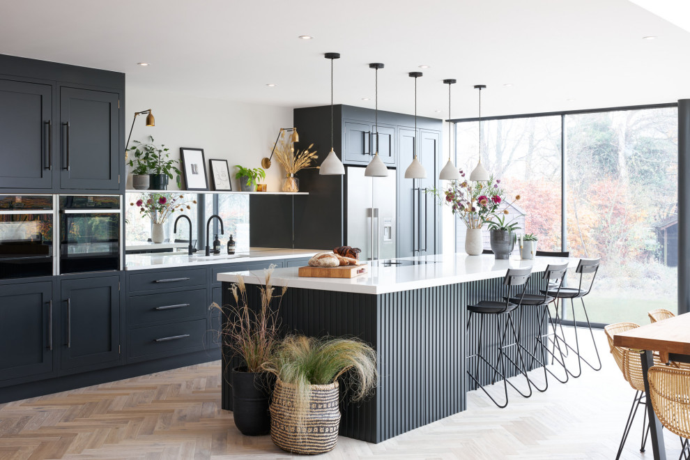 Transitional galley eat-in kitchen in London with an undermount sink, shaker cabinets, black cabinets, quartz benchtops, mirror splashback, stainless steel appliances, medium hardwood floors, with island, brown floor and white benchtop.
