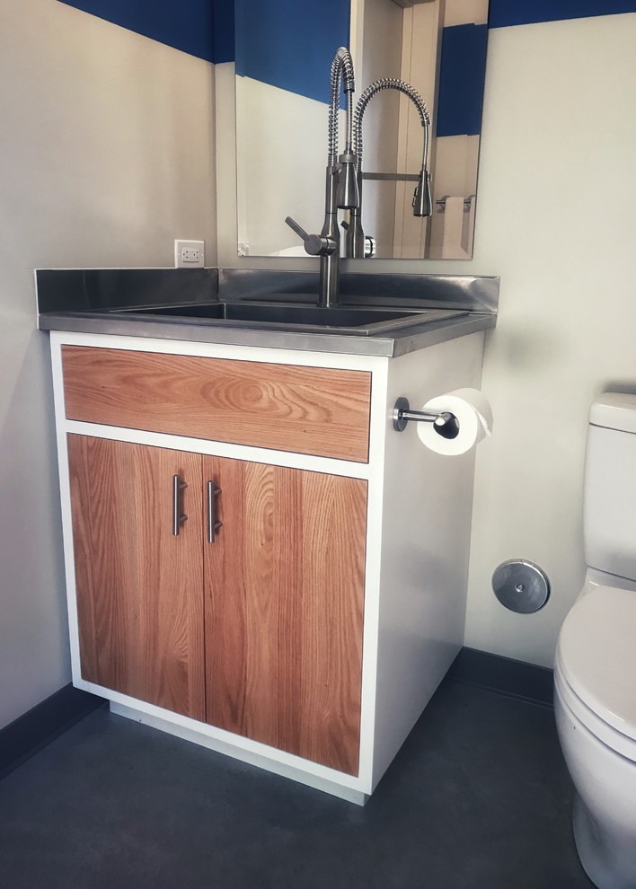 This is an example of a small industrial 3/4 bathroom in Santa Barbara with flat-panel cabinets, medium wood cabinets, a two-piece toilet, multi-coloured walls, concrete floors, stainless steel benchtops, grey floor and a drop-in sink.
