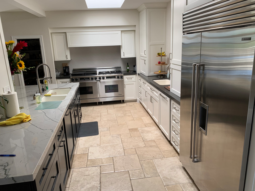 Example of a large transitional travertine floor and beige floor kitchen design in Orange County with a single-bowl sink, shaker cabinets, white cabinets, quartzite countertops, white backsplash, ceramic backsplash, stainless steel appliances, an island and black countertops