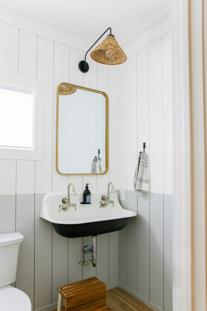 Large beach style light wood floor, brown floor and shiplap wall powder room photo in Other with black cabinets, a one-piece toilet, white walls, a wall-mount sink and a floating vanity