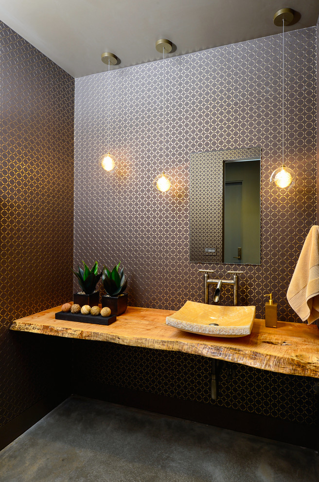This is an example of a mid-sized contemporary powder room in Other with a vessel sink, wood benchtops, multi-coloured walls, concrete floors and brown benchtops.