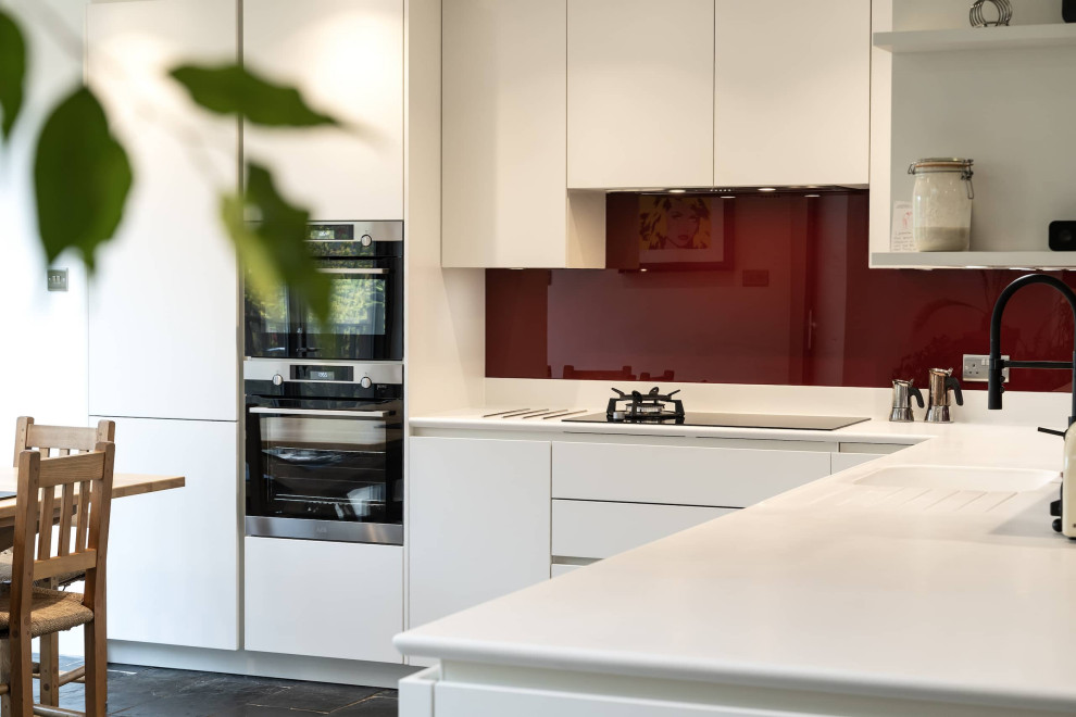 Mittelgroße Klassische Wohnküche ohne Insel in L-Form mit integriertem Waschbecken, weißen Schränken, Küchenrückwand in Rot, Glasrückwand, Küchengeräten aus Edelstahl, Keramikboden, schwarzem Boden und weißer Arbeitsplatte in Oxfordshire