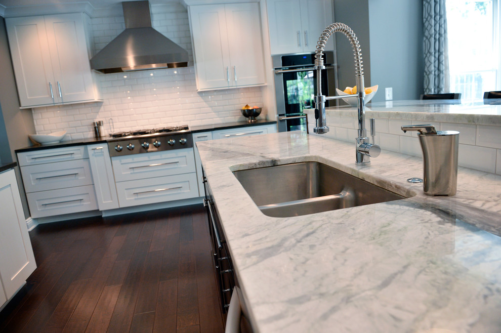 Example of a transitional dark wood floor kitchen design in Cleveland with a drop-in sink, recessed-panel cabinets, white backsplash, ceramic backsplash, stainless steel appliances and an island