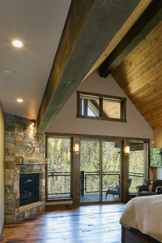 Bedroom - large rustic master medium tone wood floor and brown floor bedroom idea with beige walls, a corner fireplace and a stone fireplace
