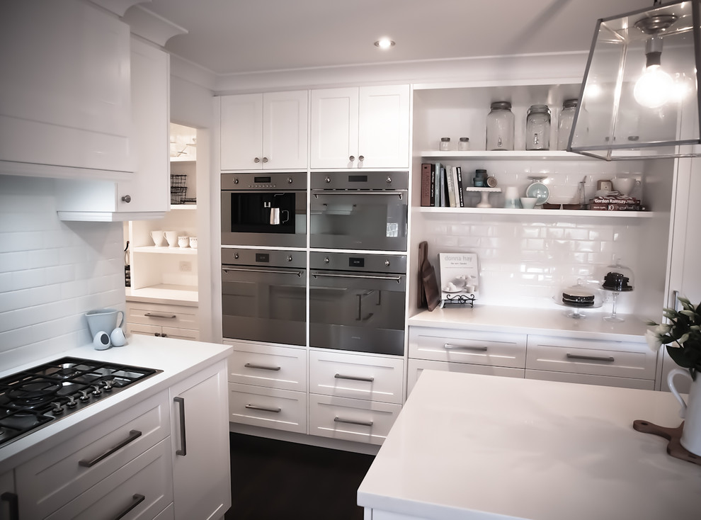 Design ideas for a mid-sized traditional kitchen in Wollongong with a farmhouse sink, shaker cabinets, white cabinets, quartz benchtops, white splashback, subway tile splashback, stainless steel appliances, dark hardwood floors and with island.