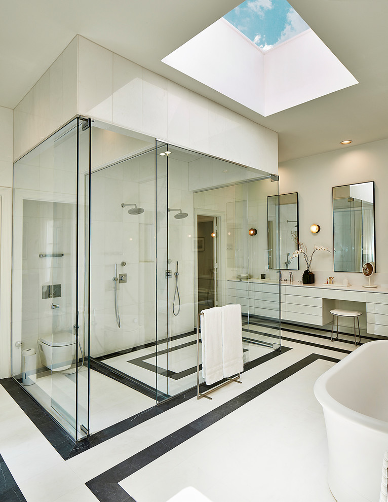 Design ideas for an expansive modern master bathroom in Dallas with flat-panel cabinets, white cabinets, a freestanding tub, a curbless shower, a wall-mount toilet, black and white tile, glass sheet wall, white walls, marble floors, an integrated sink, quartzite benchtops, white floor and a hinged shower door.