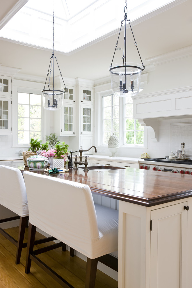 Traditional kitchen in DC Metro with an undermount sink, glass-front cabinets, white cabinets and wood benchtops.