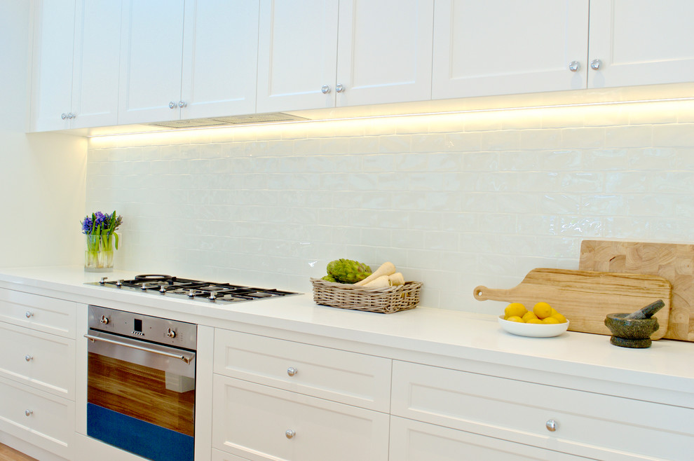 This is an example of a mid-sized beach style l-shaped eat-in kitchen in Sydney with a farmhouse sink, shaker cabinets, white cabinets, wood benchtops, white splashback, subway tile splashback, stainless steel appliances, medium hardwood floors and with island.