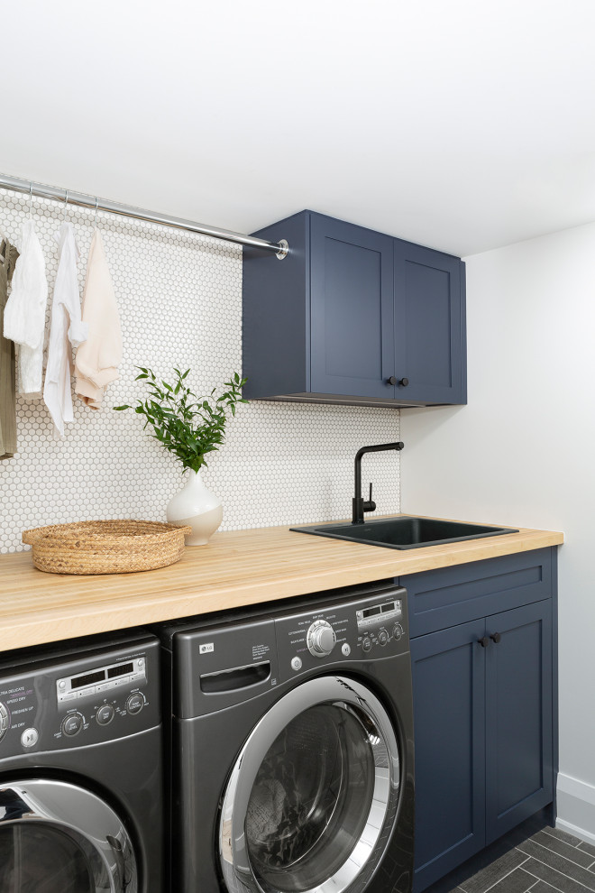 Inspiration for a modern laundry room in Toronto with a drop-in sink, shaker cabinets, blue cabinets, wood benchtops, white splashback, ceramic splashback, white walls, porcelain floors and grey floor.