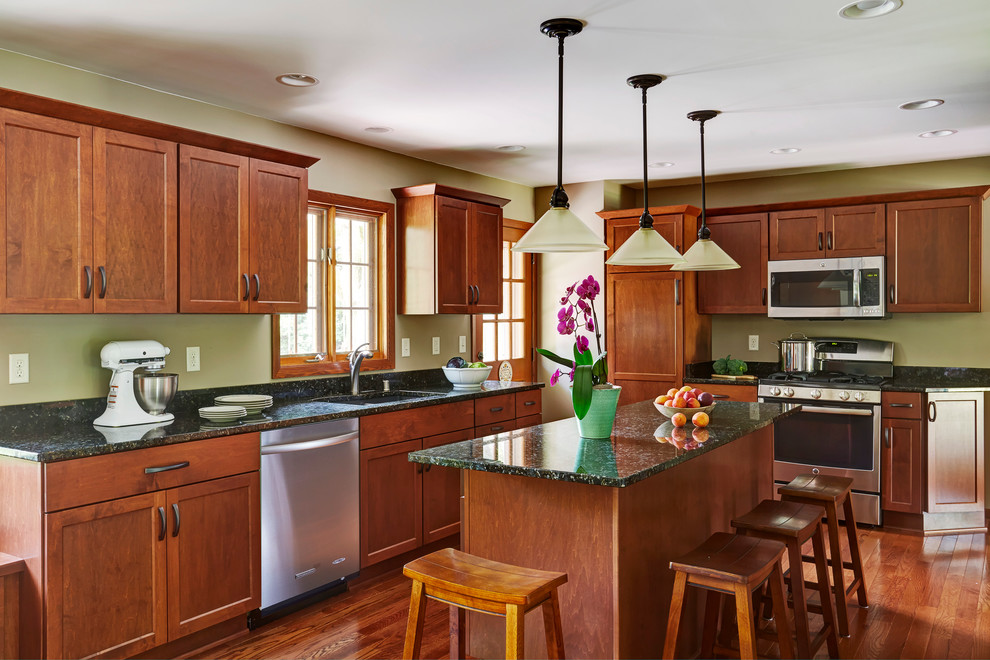 Inspiration for a large transitional l-shaped medium tone wood floor eat-in kitchen remodel in Milwaukee with an undermount sink, shaker cabinets, medium tone wood cabinets, granite countertops, green backsplash, stone slab backsplash, stainless steel appliances and an island
