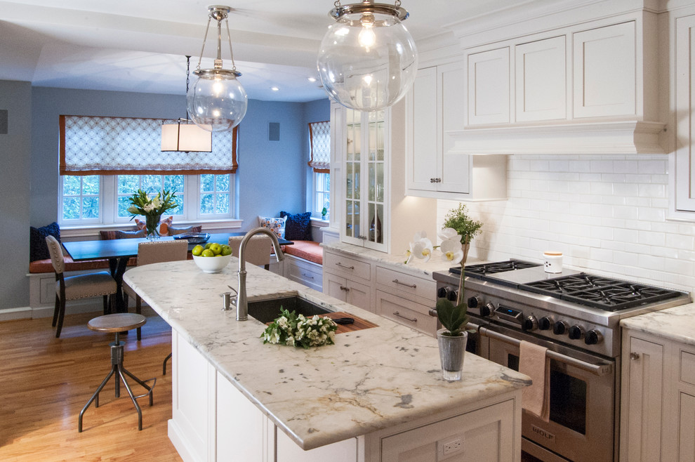 Inspiration for a mid-sized transitional l-shaped eat-in kitchen in Philadelphia with an undermount sink, shaker cabinets, white cabinets, white splashback, ceramic splashback, stainless steel appliances, medium hardwood floors, with island and quartzite benchtops.