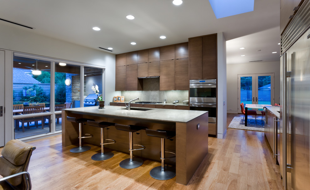 Photo of a contemporary l-shaped eat-in kitchen in Dallas with an integrated sink, flat-panel cabinets, dark wood cabinets, granite benchtops, grey splashback, stone slab splashback, stainless steel appliances, medium hardwood floors and with island.