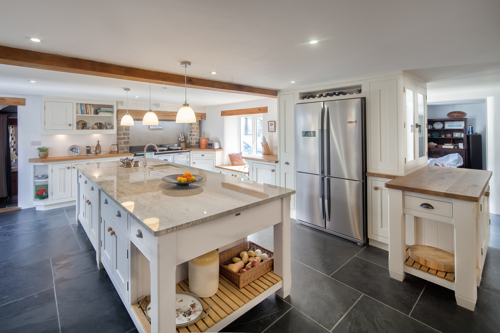 This is an example of a large country single-wall kitchen in Cornwall with an undermount sink, shaker cabinets, beige cabinets, concrete benchtops, grey splashback, ceramic splashback, stainless steel appliances, concrete floors, with island and black floor.