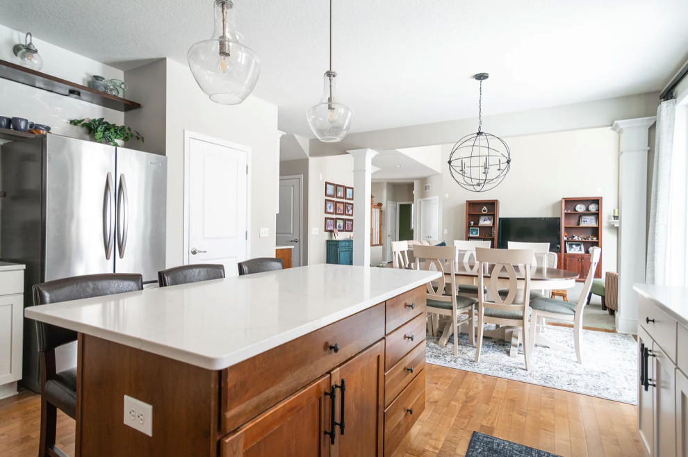 Eat-in kitchen - large transitional u-shaped medium tone wood floor and brown floor eat-in kitchen idea in Minneapolis with a single-bowl sink, shaker cabinets, white cabinets, quartz countertops, white backsplash, porcelain backsplash, stainless steel appliances, an island and white countertops