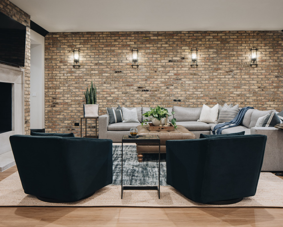This is an example of a large transitional fully buried basement in Chicago with grey walls, light hardwood floors, a standard fireplace, a concrete fireplace surround, brown floor and brick walls.