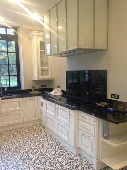 This is an example of a large traditional l-shaped separate kitchen in Other with an integrated sink, white cabinets, granite benchtops, black splashback, granite splashback, panelled appliances, cement tiles, multi-coloured floor and black benchtop.
