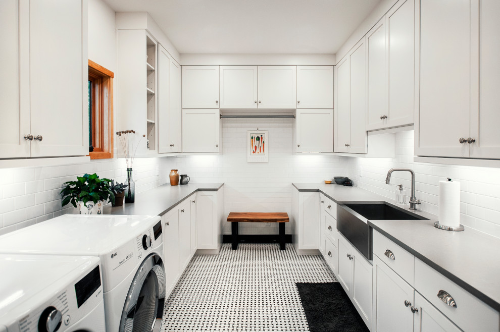 Idéer för stora amerikanska u-formade grått tvättstugor enbart för tvätt, med en rustik diskho, skåp i shakerstil, vita skåp, bänkskiva i kvarts, vitt stänkskydd, stänkskydd i tunnelbanekakel, vita väggar, klinkergolv i keramik, en tvättmaskin och torktumlare bredvid varandra och svart golv