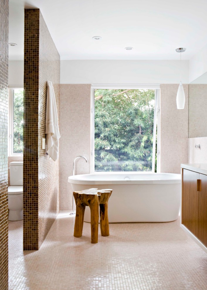This is an example of a midcentury bathroom in Los Angeles with flat-panel cabinets, medium wood cabinets, a freestanding tub, a two-piece toilet, beige tile, mosaic tile, white walls and mosaic tile floors.