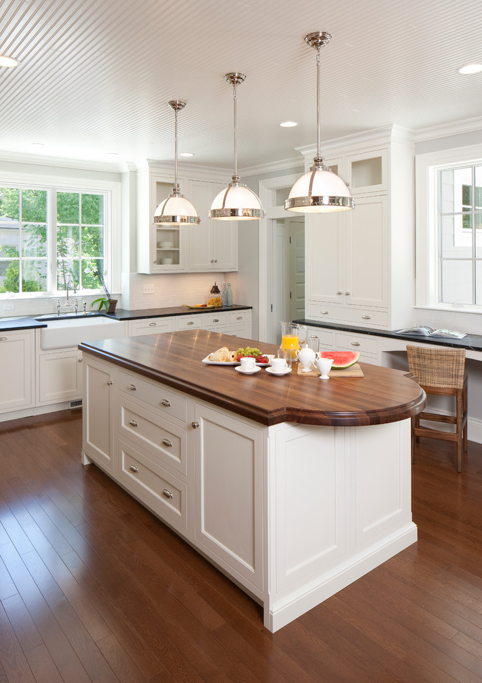 Inspiration for a traditional u-shaped kitchen in Grand Rapids with a farmhouse sink, shaker cabinets, white cabinets, wood benchtops, white splashback, subway tile splashback, medium hardwood floors and with island.